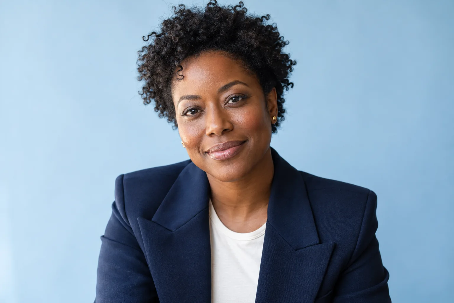 Confident Black woman with natural curls and a navy blazer, photographed in soft studio light